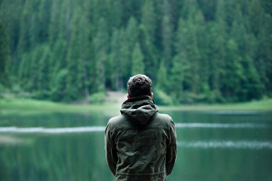 man in green hoddie overlooking lake with trees in background man in green hoddie overlooking lake with trees in background