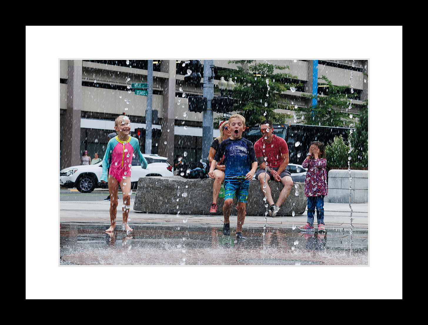 Boy yelling joyfully in Boston splash fountain while others play around him under water jets.