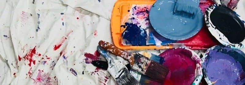 assorted-color paints and paintbrushes on white tarp