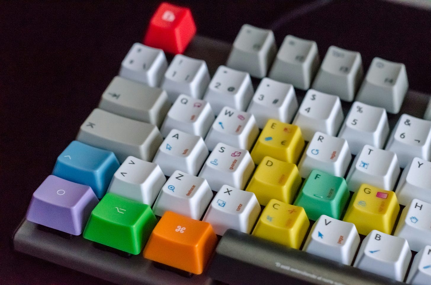 Close-up view of a mechanical keyboard with custom keycaps in various bright colors including red, yellow, green, blue, purple, and orange scattered among white keycaps, creating a colorful accent pattern against the dark keyboard base. Close-up view of a mechanical keyboard with custom keycaps in various bright colors including red, yellow, green, blue, purple, and orange scattered among white keycaps, creating a colorful accent pattern against the dark keyboard base.
