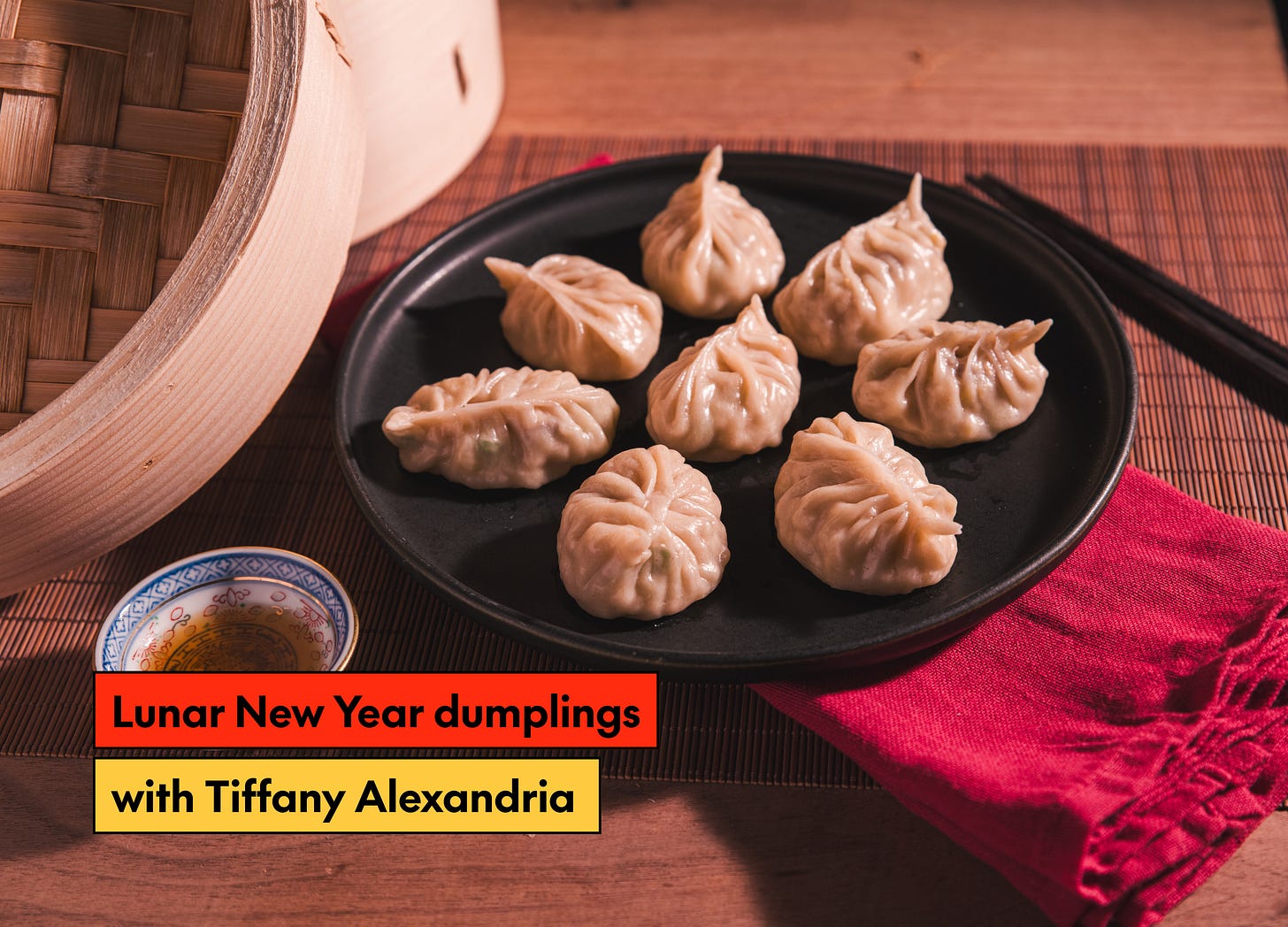 Beautifully pleated dumplings sit on a black plate with a steamer in the background and the text "Lunar New Year dumplings with Tiffany Alexandria"