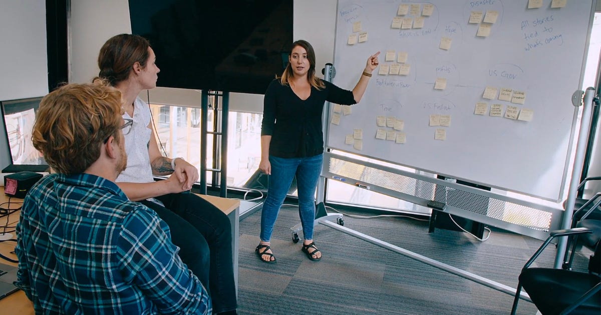 Three investigative journalists confer over a whiteboard filled with sticky notes, in a scene from The Grab that tries to build a sense of suspense.