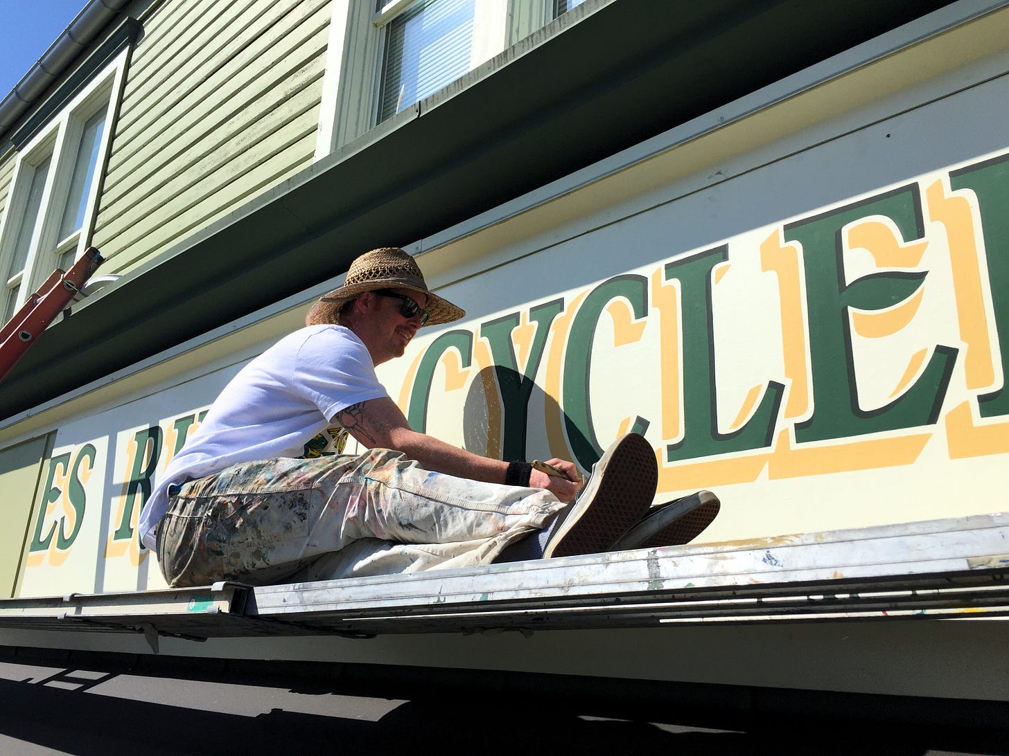 sign painter Ira Coyne balances on a ledge, brush in hand, touching up some yellow and green letters above a storefront sign painter Ira Coyne balances on a ledge, brush in hand, touching up some yellow and green letters above a storefront