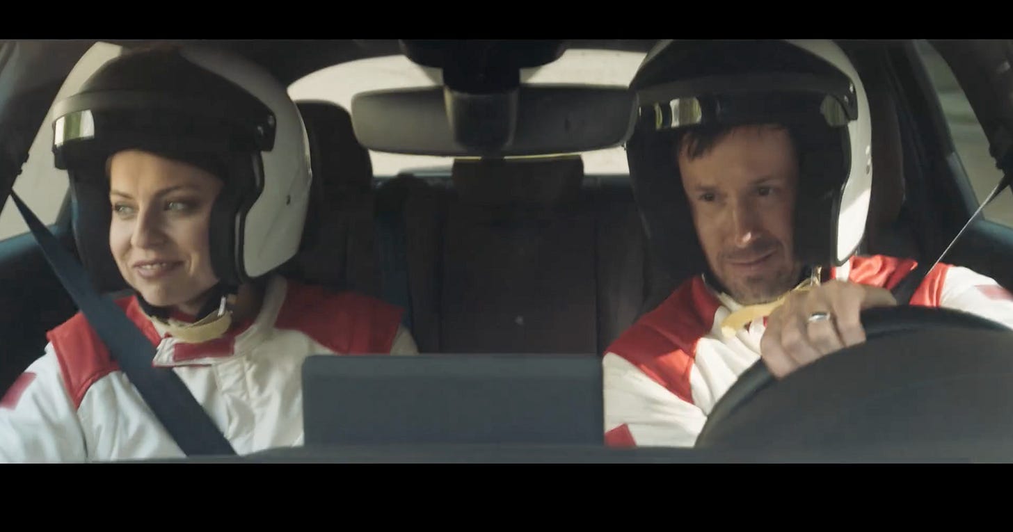 Spurgeon and her costar wearing racing outfits while riding in a car.