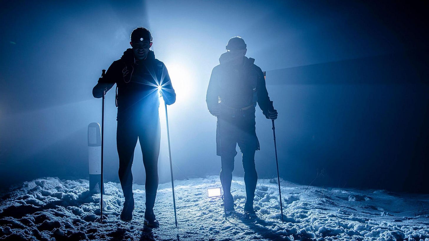 Two racers with running poles on snow and silhouetted against a bright back light during nightfall Two racers with running poles on snow and silhouetted against a bright back light during nightfall
