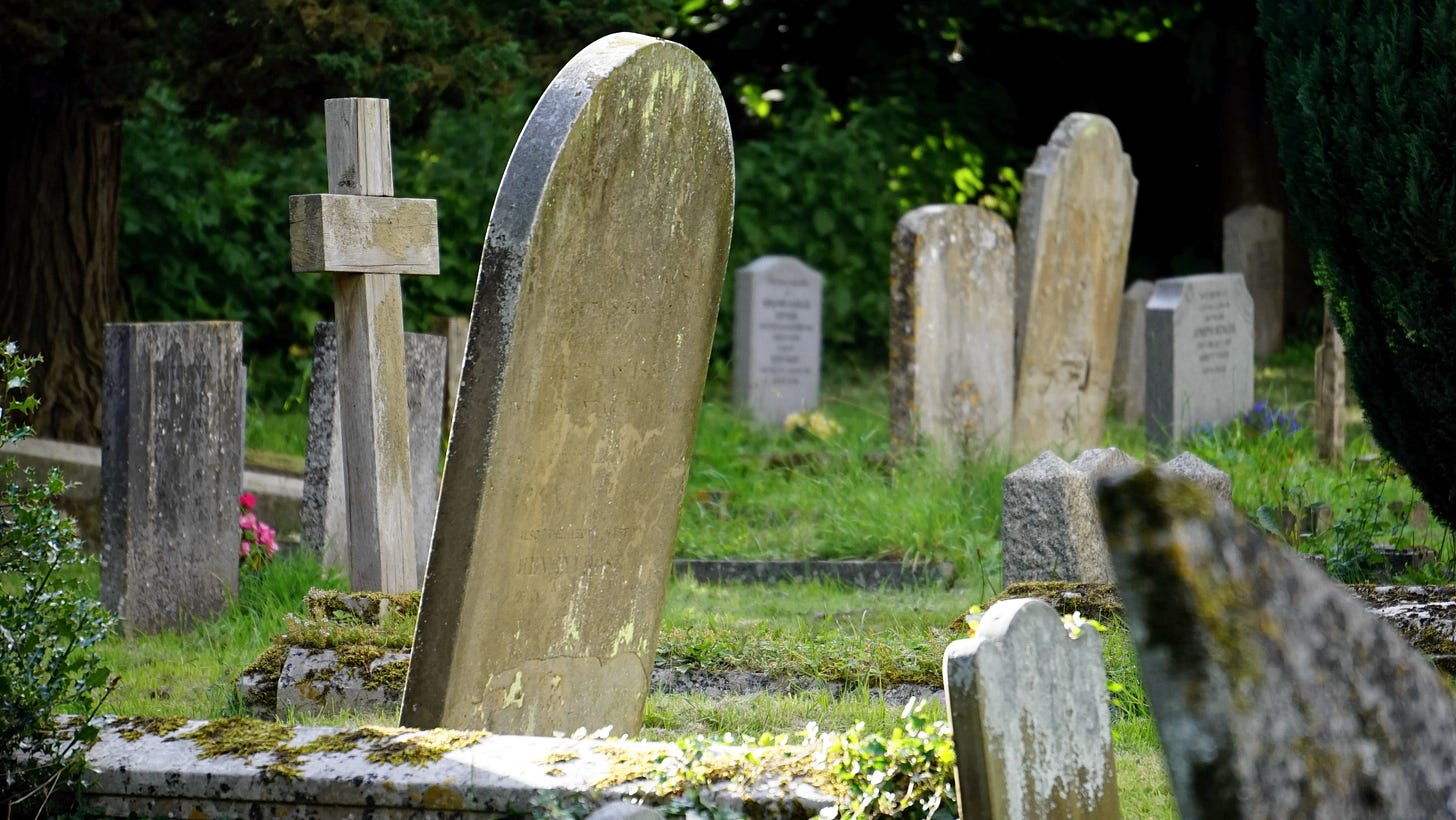 A tombstone leans over a grassy graveyard