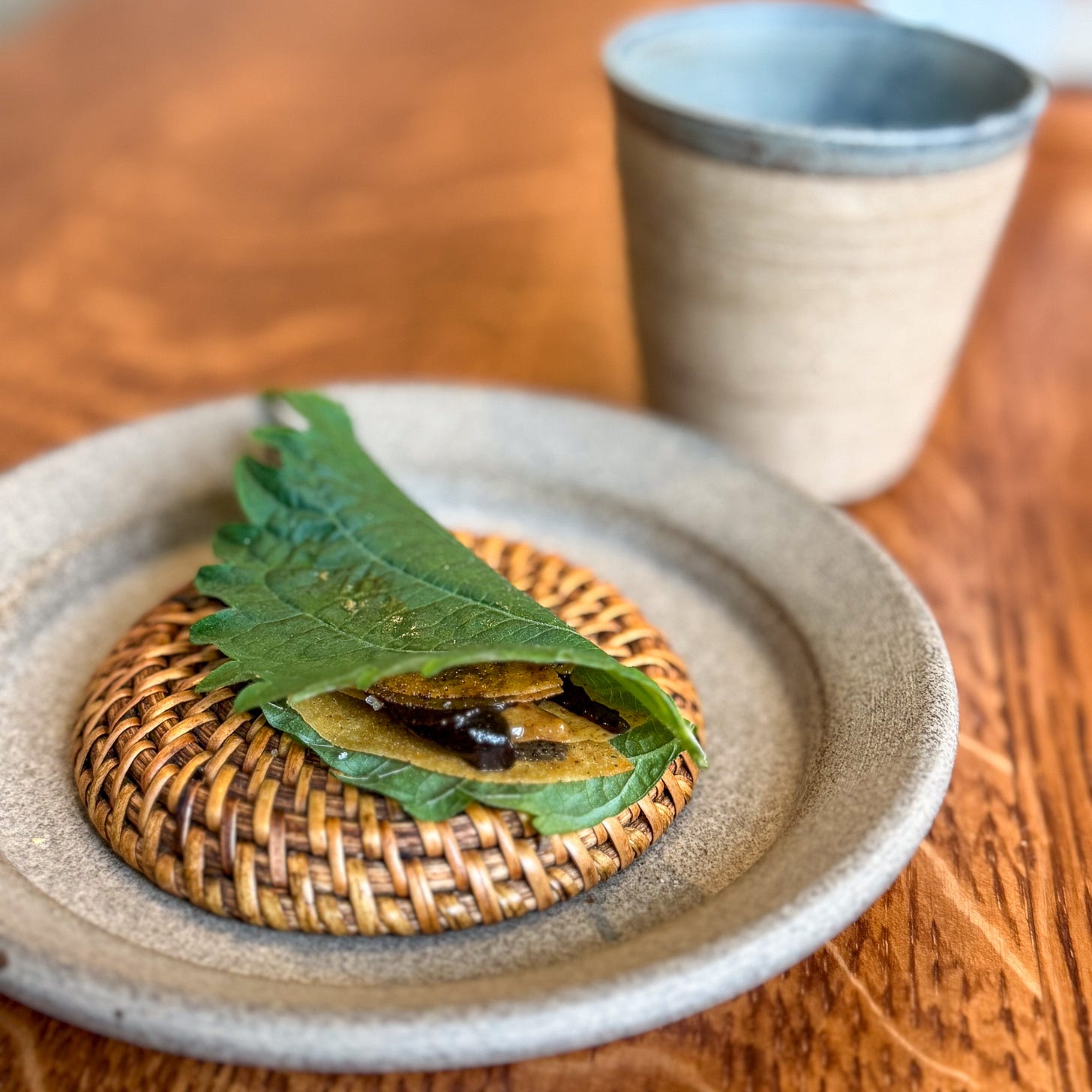 Shiso leaf with black garlic and chicken skin at Eme, Paris 4th — opening course on woven ceramic plate