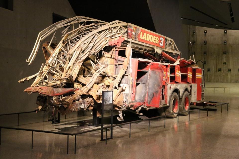 This element opens a lightbox image gallery - The heavily damaged truck of FDNY Ladder Company 3 stands in the Museum’s Foundation Hall. The front of the truck is completely gone and much of what remains is twisted hunks of metal.