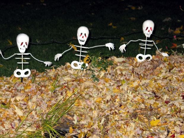three toy skeletons standing in a pile of leaves at night suggesting a murder
