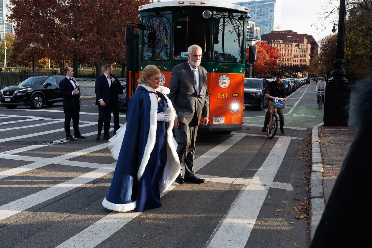 wedding couple exits a trolley and crosses a street with fall trees behind them