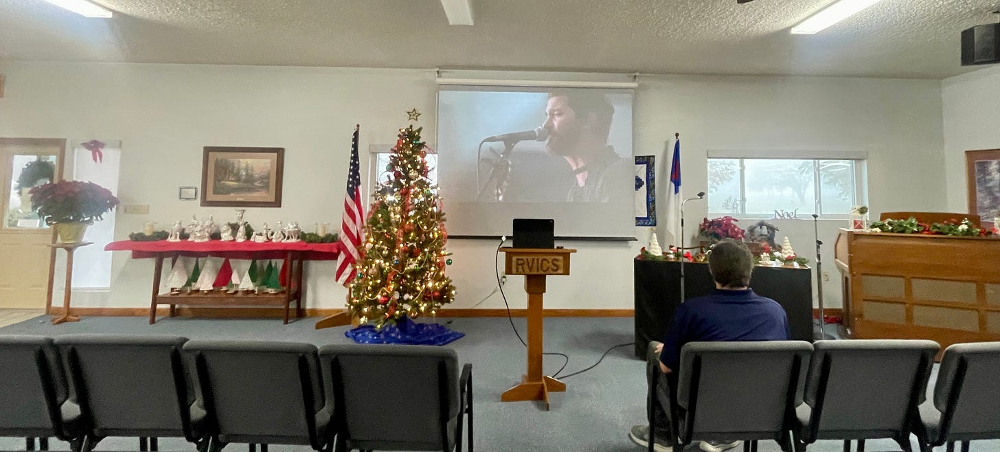 Photo of Tommy sitting in the front of the decorated room with a beautiful Christmas tree. He as making sure his sound system and video of Christian music worked well. Photo of Tommy sitting in the front of the decorated room with a beautiful Christmas tree. He as making sure his sound system and video of Christian music worked well.