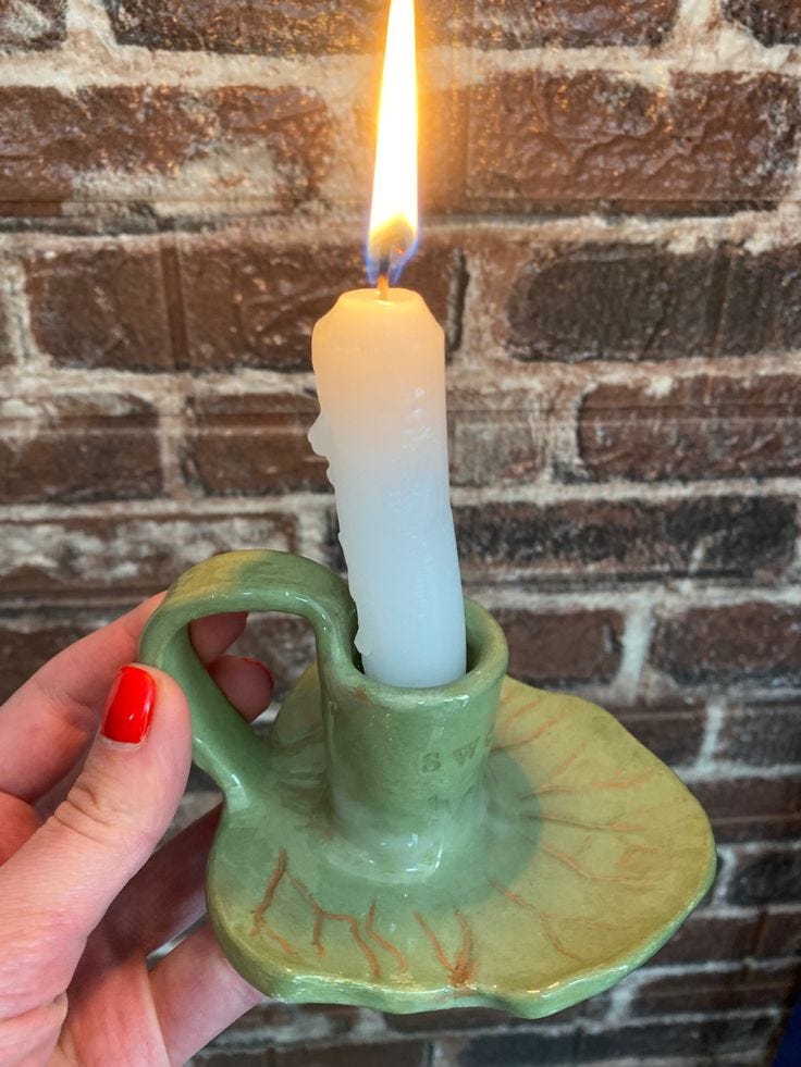 This may contain: a person holding a small candle in a green cup with a saucer on it
