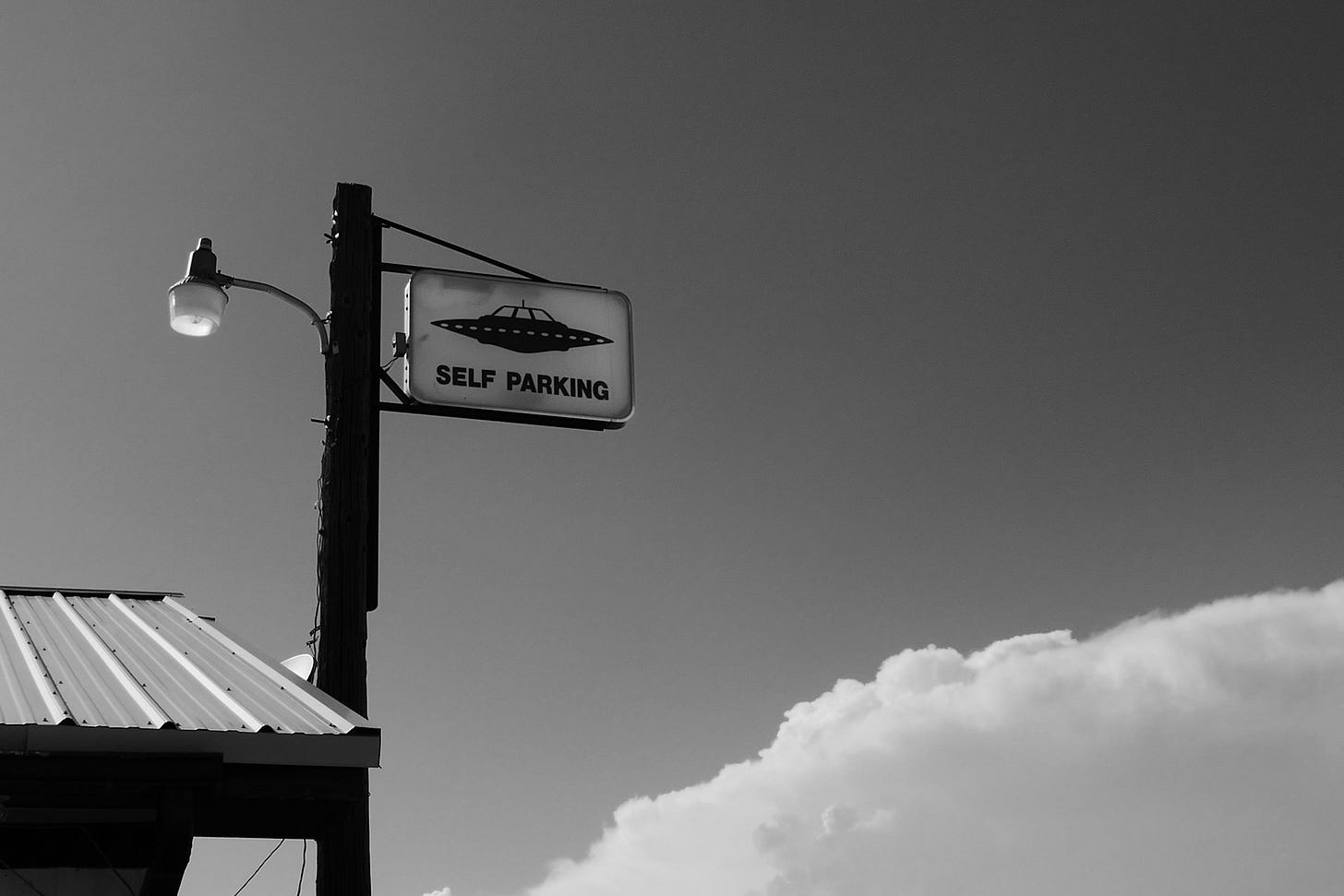 a grey scale photo of a post beside a roof which has a lamp and UFO self parking sign a grey scale photo of a post beside a roof which has a lamp and UFO self parking sign
