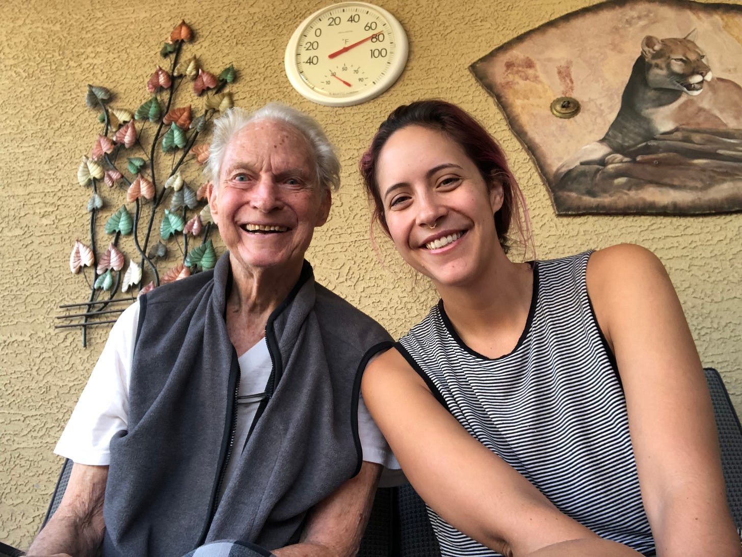 A 70-something-year-old man smiles for a photo with his 30-something-year-old granddaughter.