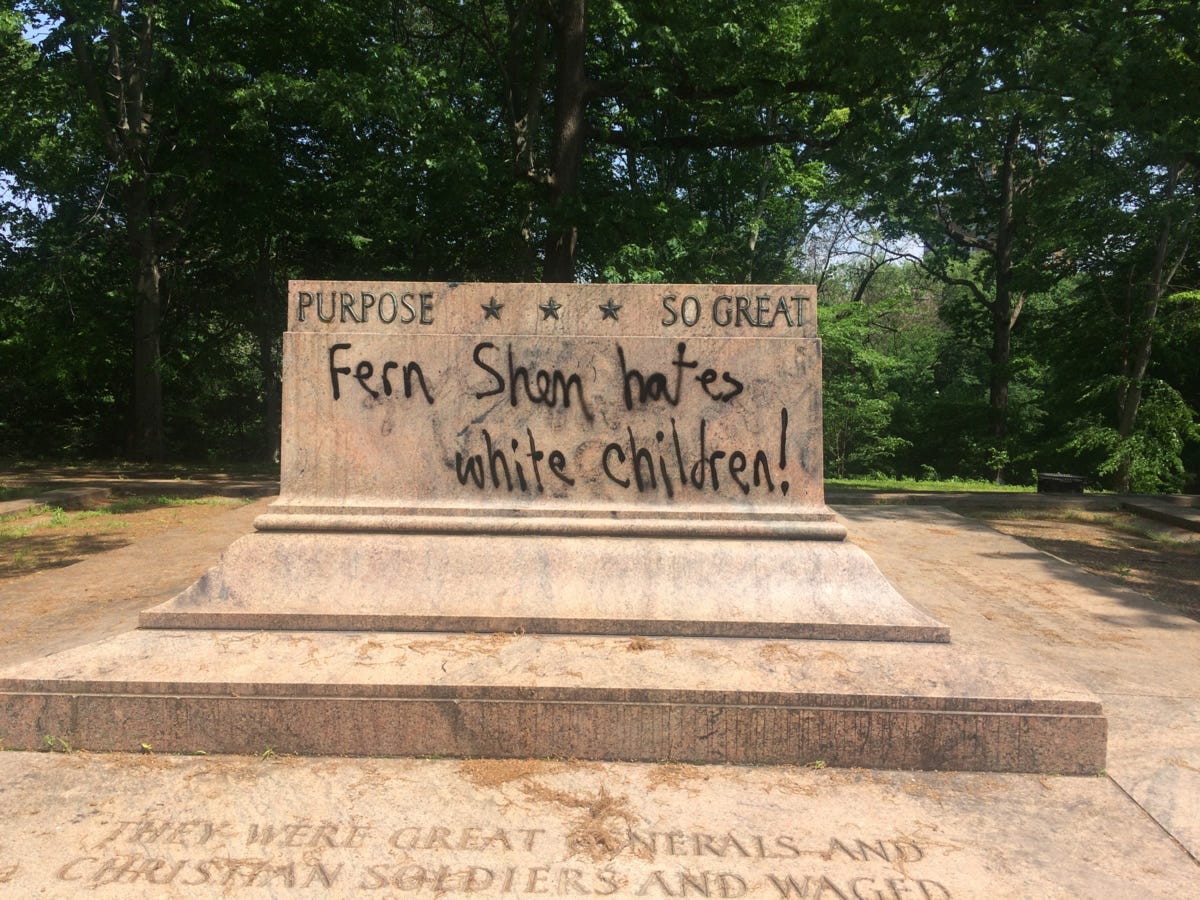 An empty plinth displaying the slogan in black spray paint, "Fern Shen hates white children." An empty plinth displaying the slogan in black spray paint, "Fern Shen hates white children."