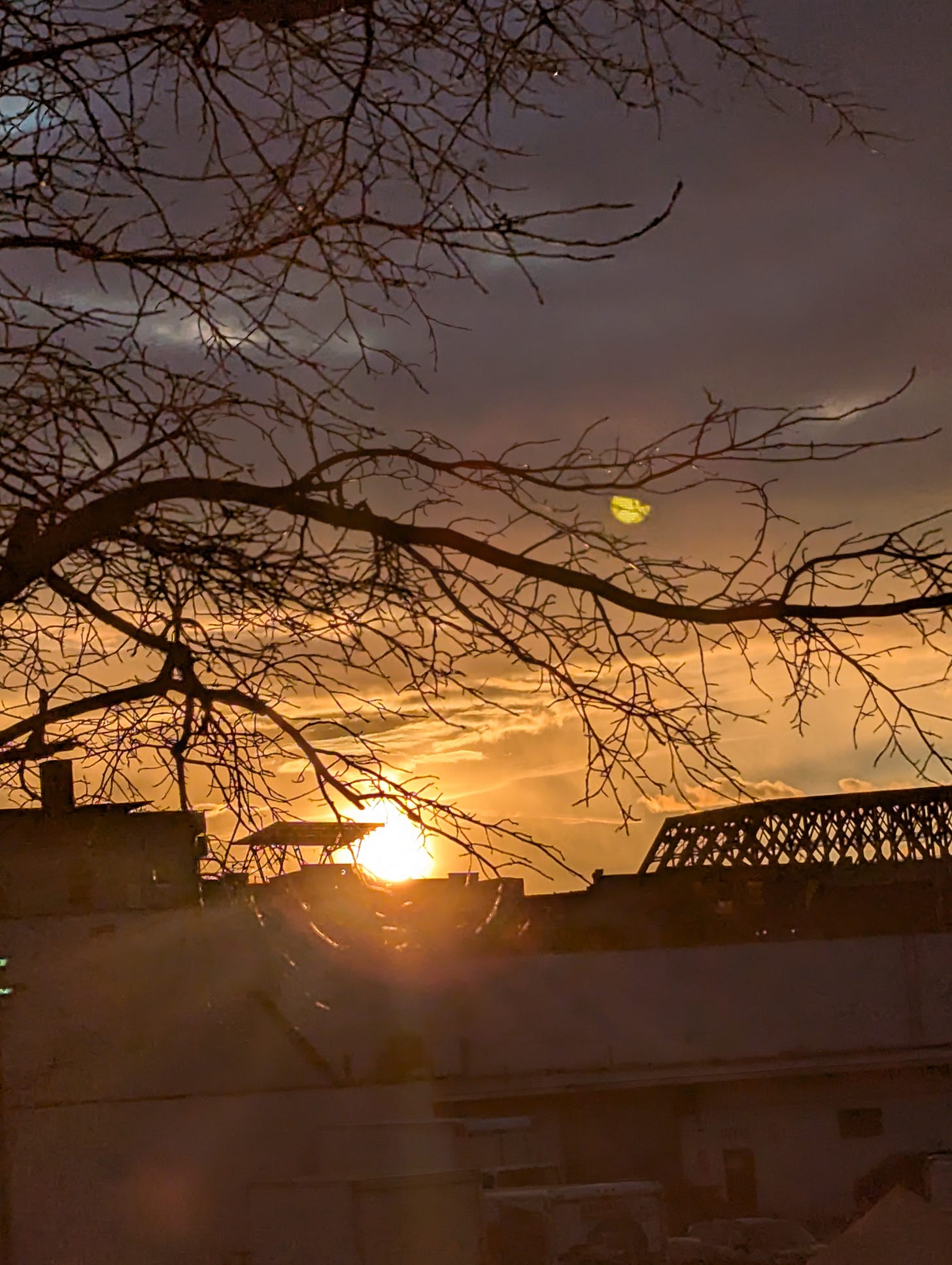 Fiercely orange sunset against a multihued sky with a bridge and buildings in the foreground.