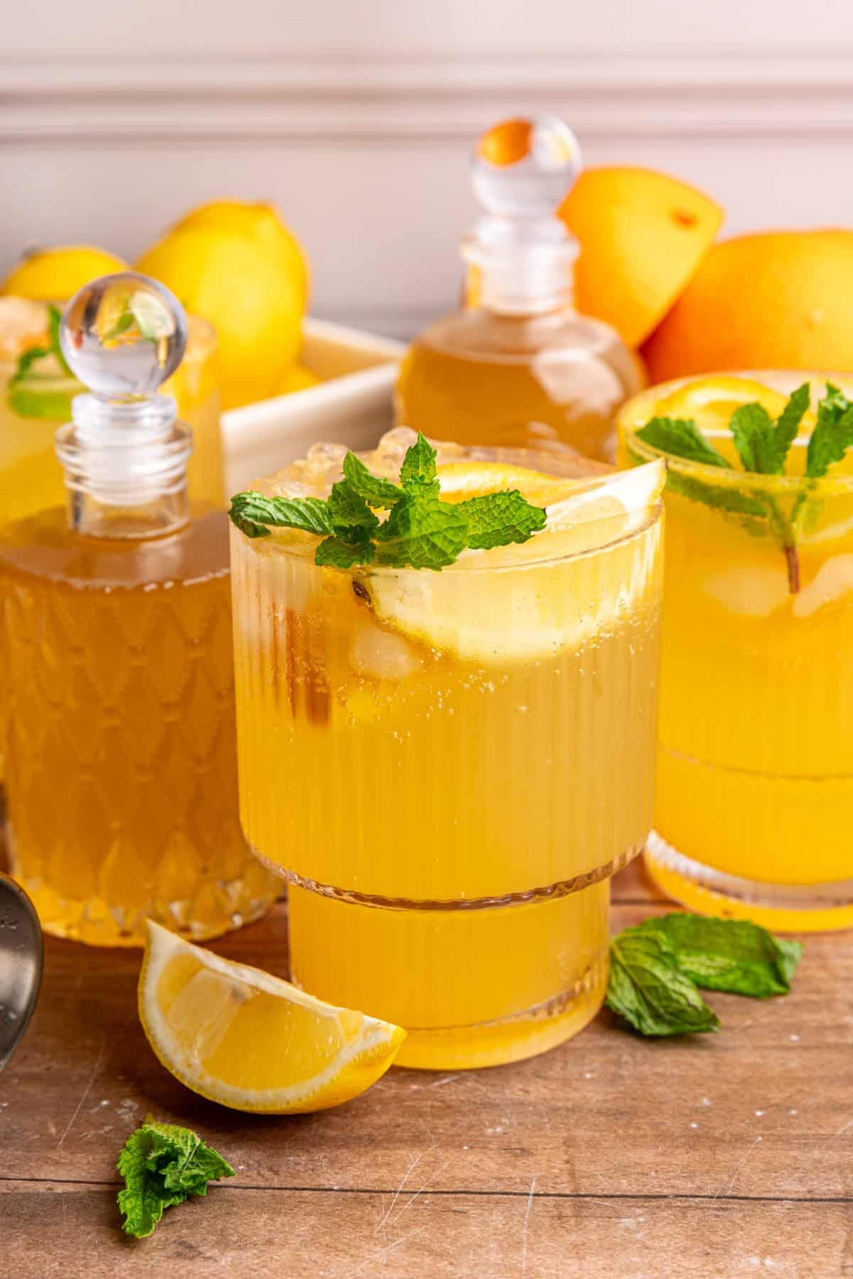 A few glasses of citrus mocktail on a table with jars of lemon ginger syrup.