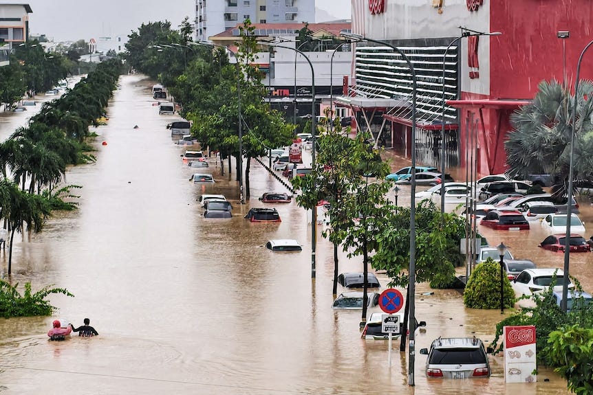 People wade through brown floodwaters near inundated vehicles in Vietnam.