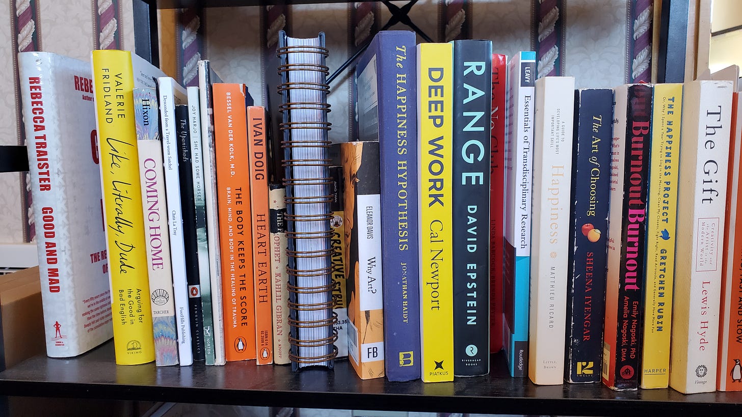A photo of a shelf full of books. Titles include: Good and Mad; Like, Literally, Dude; Descended from a Travel-Worn Satchel; The Upanishads: She Had Some Horses; The Body Keeps the Score; The Prophet; Creative Struggle; Why Art; The Happiness Hypothesis; Deep Work; Range; The No Club; Essentials of Transdisciplinary Research; Happiness; The Art of Choosing; Burnout; The Happiness Project; The Gift; Thinking, Fast and Slow; Radical Hope; Our Souls at Night