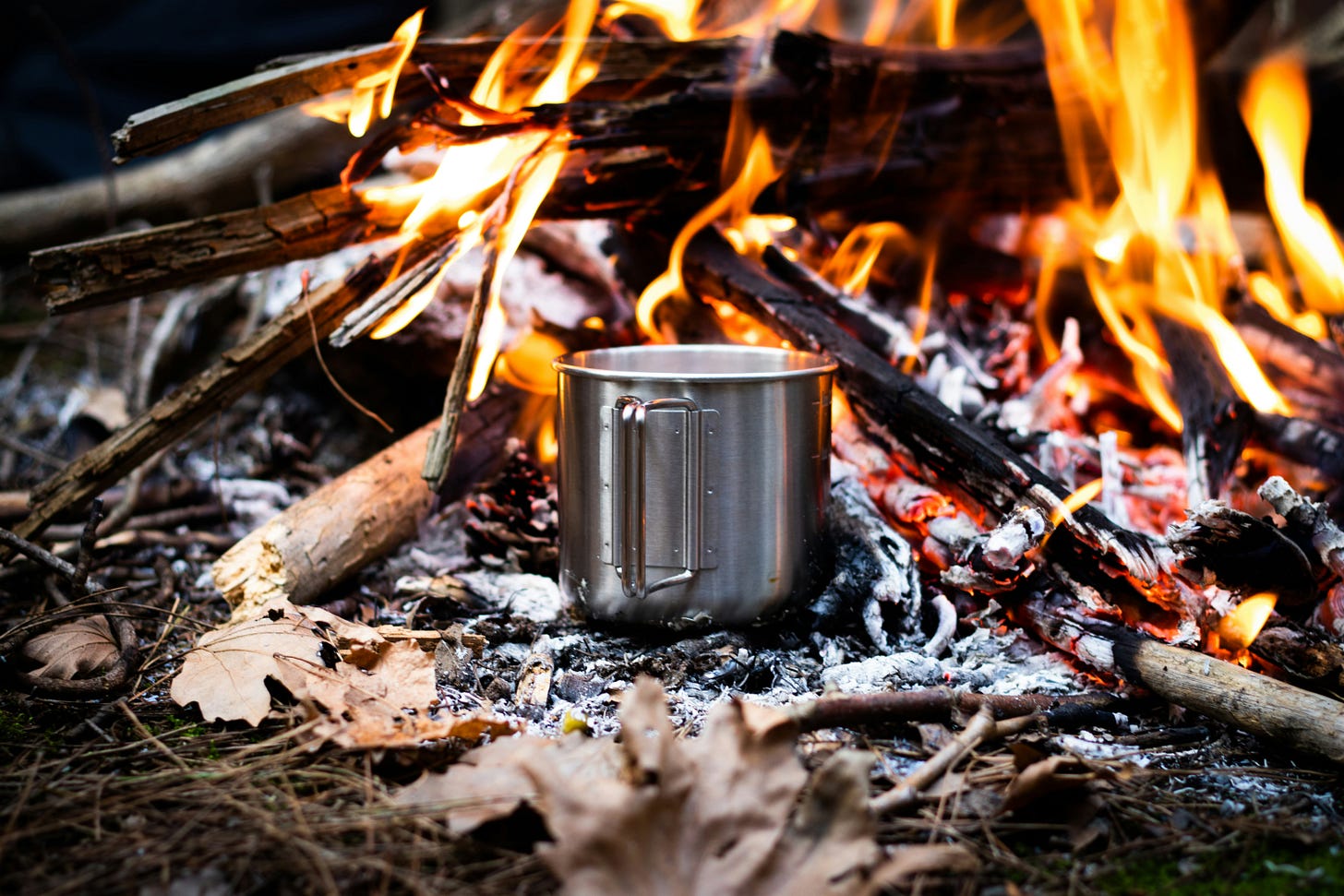 Metal camping mug being heated over campfire flames, representing the reality of boiling water for safe drinking in Indigenous communities under long-term water advisories