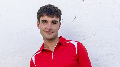 Rory wears a red polo shirt and is stood against a whitewashed wall