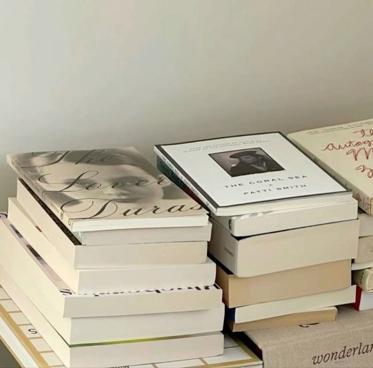 This may contain: a stack of books sitting on top of each other next to a white vase with flowers in it