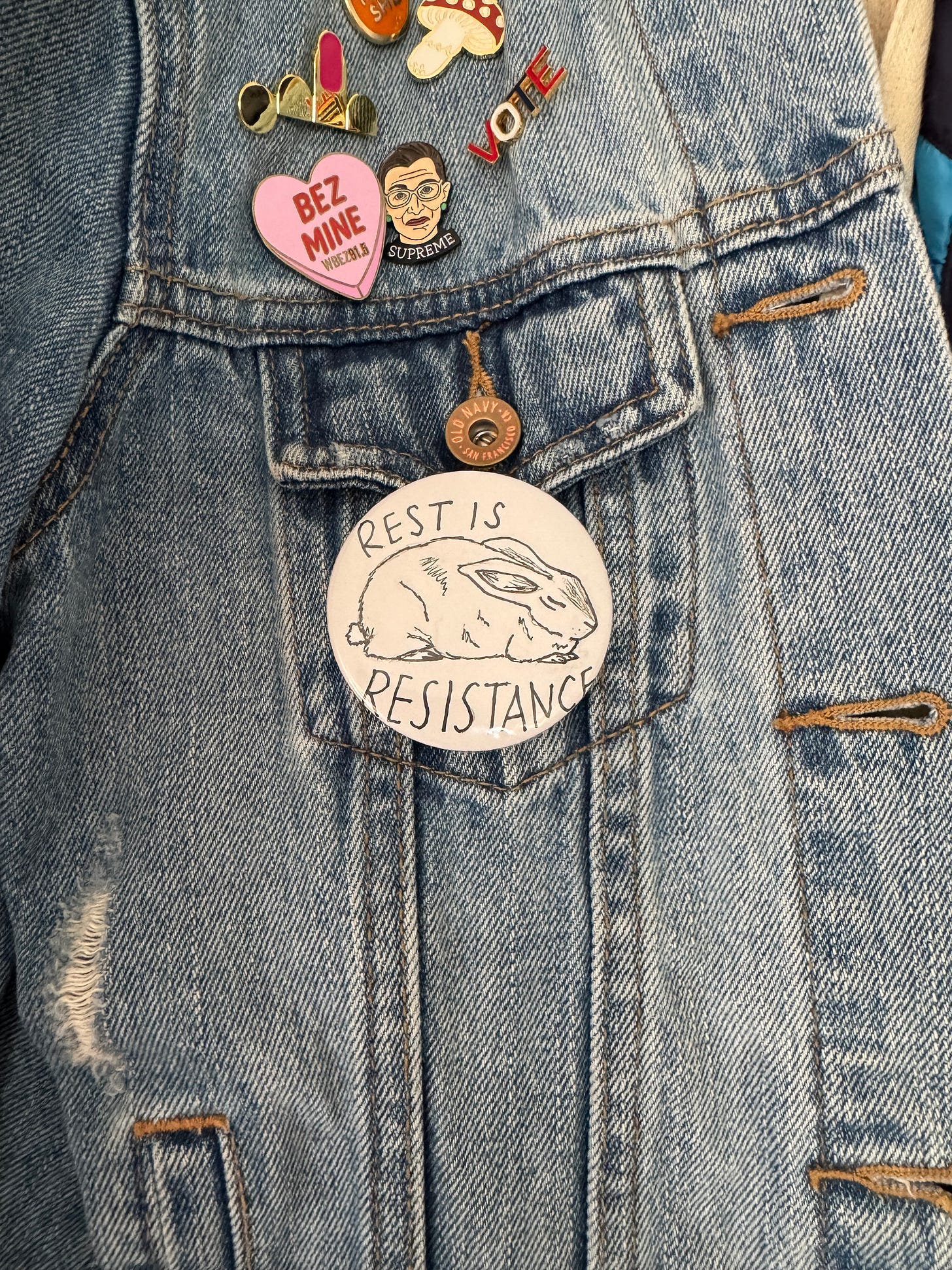 a button on a jean jacket with a sleeping rabbit, that says "rest is resistance"