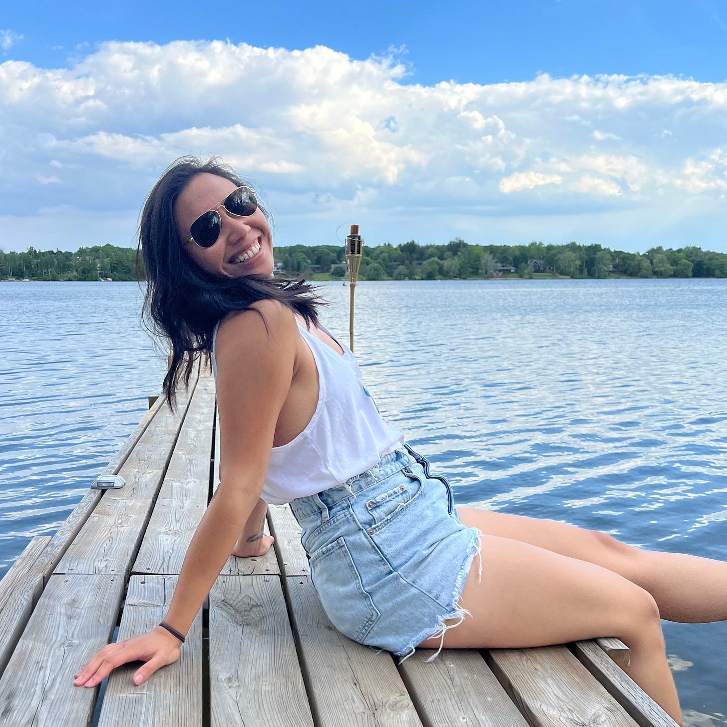 Justine sitting on a dock with a lake and trees in the background.