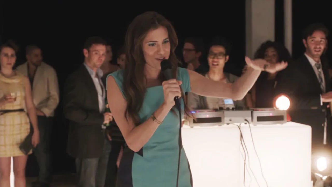 Marnie of HBO's Girls sings into a microphone at crowded event.