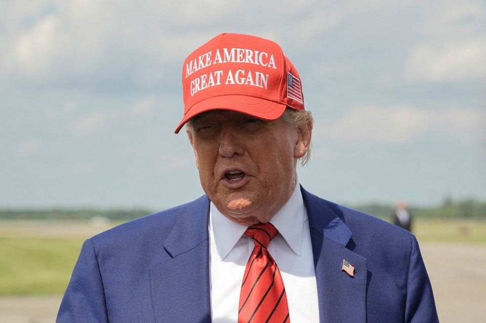 Donald Trump speaking, wearing a "Make America Great Again" hat.