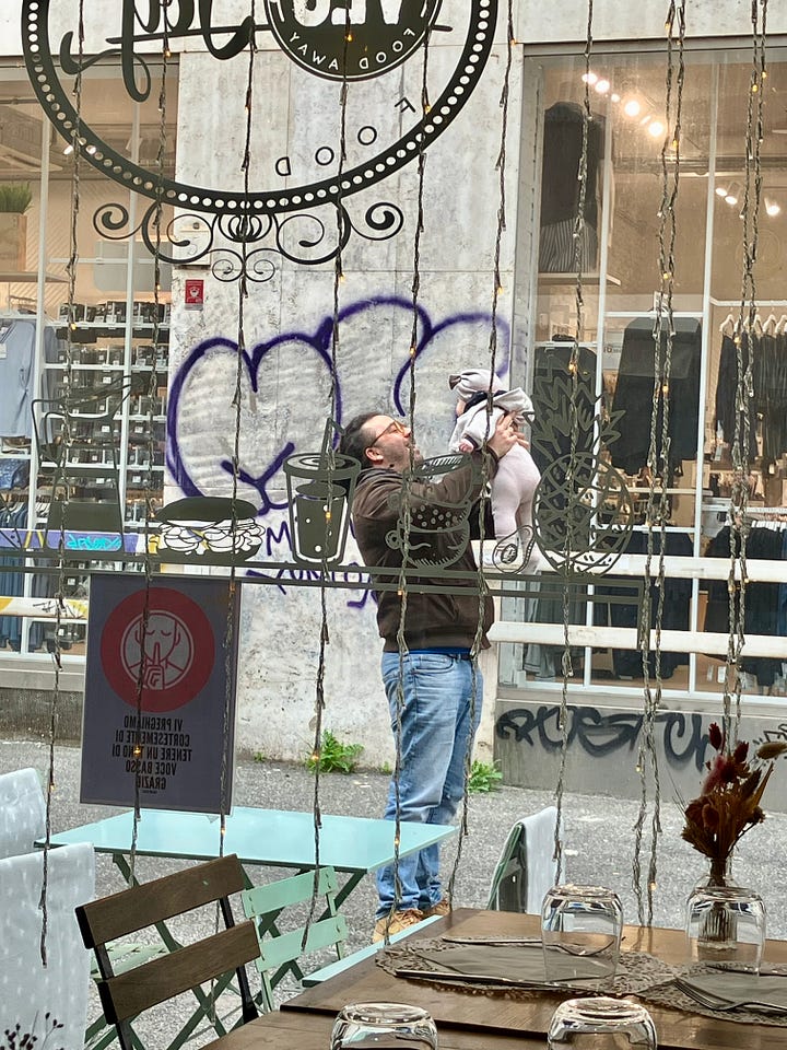 Collage di quattro scatti. Una bambina, Elena, pranza al ristorante con il papà. Un papà, con lo zaino della figlia in spalla, la accompagna all’ingresso della scuola. Tre bambini di spalle camminano verso l’ingresso della scuola con la mamma. Un altro papà solleva la sua bambina, piccola piccola, davanti alla vetrina di un locale. È un momento di immensa tenerezza.