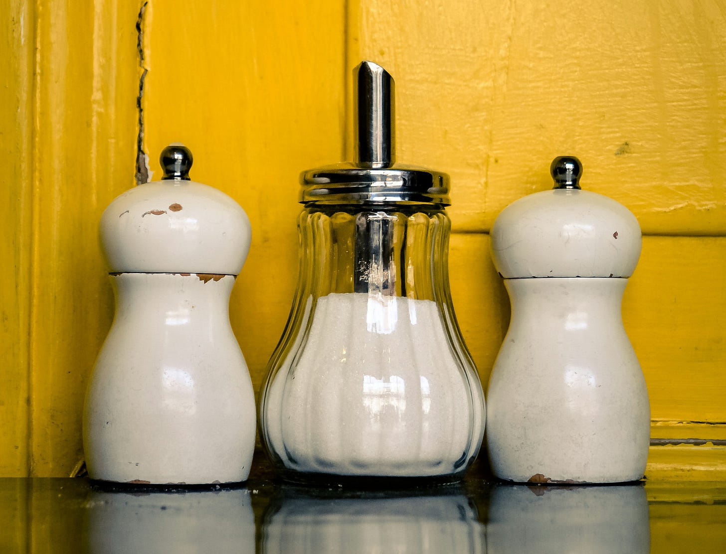 three salt shakers on a counter in front of a yellow wall