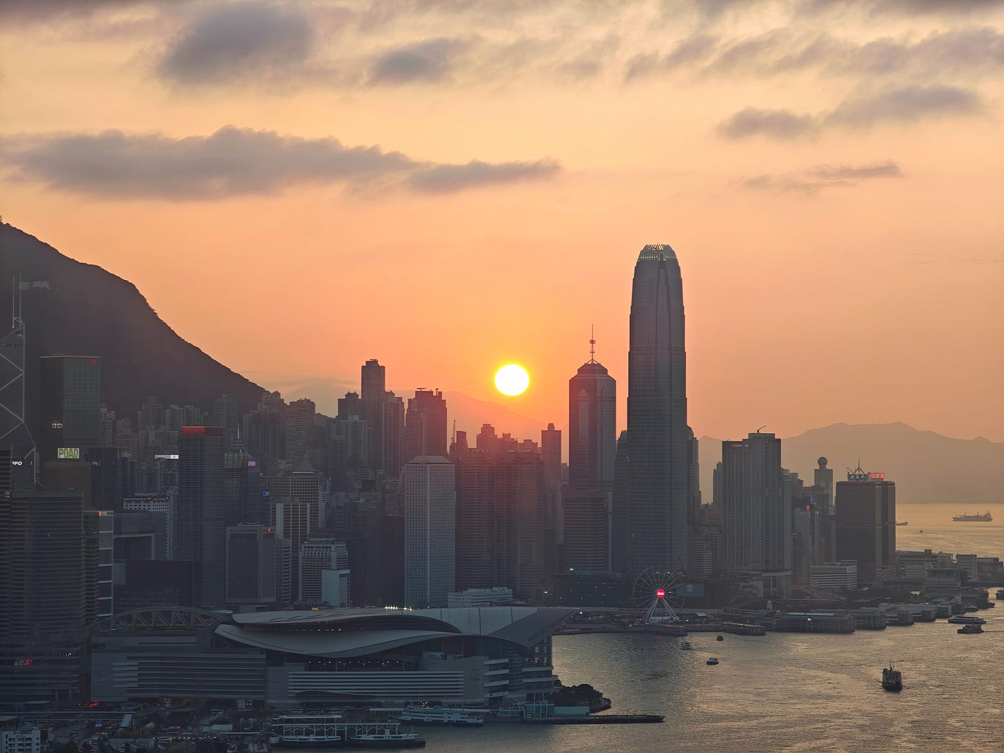 表裡見聞錄：黃昏時分，阿芒從紅香爐峰俯瞰維港 IFC，中環摩天大樓沐浴在落日餘暉中。世人迷戀表界那片閃爍的黃金海面，但在裡界視角，那不過是被龐大資本系統無聲揉碎、等待被贖回的時間。