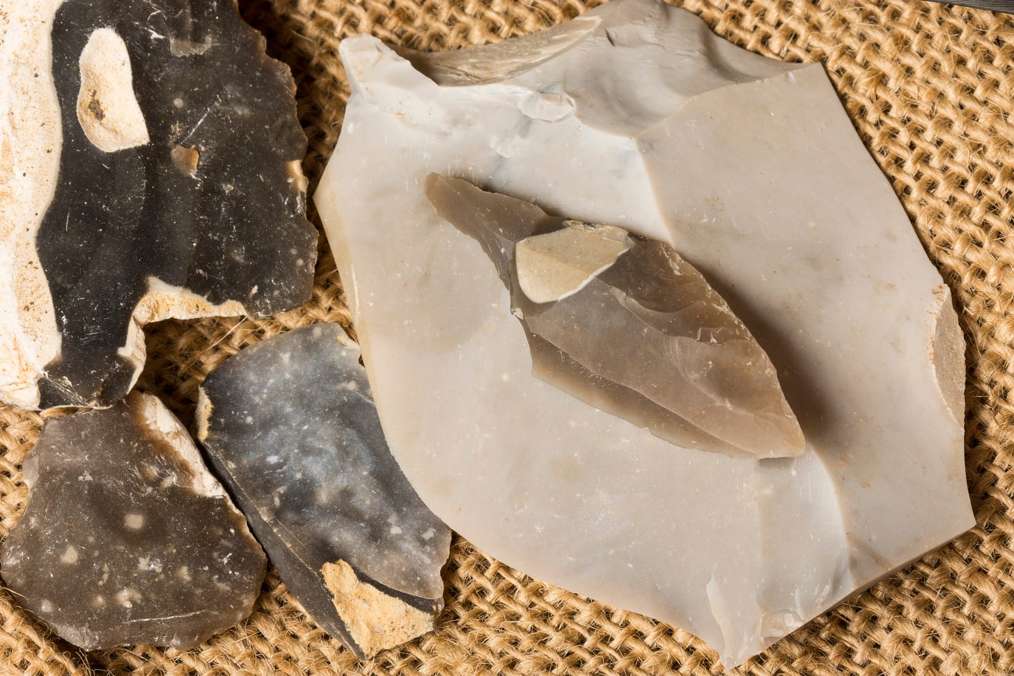 Several pieces of flint stone with sharp edges are displayed on a piece of burlap fabric.