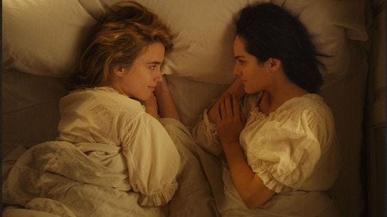 This may contain: two women laying in bed next to each other and one is touching her face with her hand