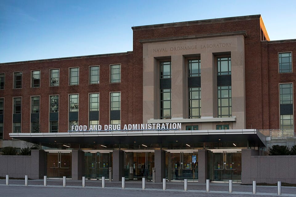 Photograph of the front facade of the US Food and Drug Administration's Building 1, part of the FDA's White Oak campus. The three-story brick building is faced with a sandstone slab on the front identifying at as the "Naval Ordnance Laboratory," the building's previous function.