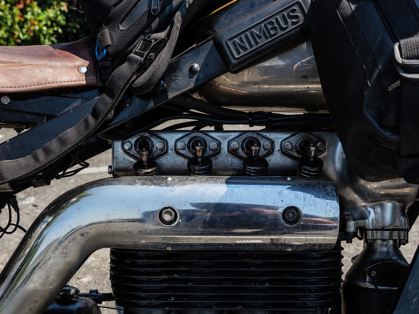 Close-up photo of the Nimbus motorcycle engine. There are black cooling fins on the cylinders, and a chrome exhaust manifold. Atop the cylinders are the exposed valvetrain springs and arms. This is obviously a very old design.