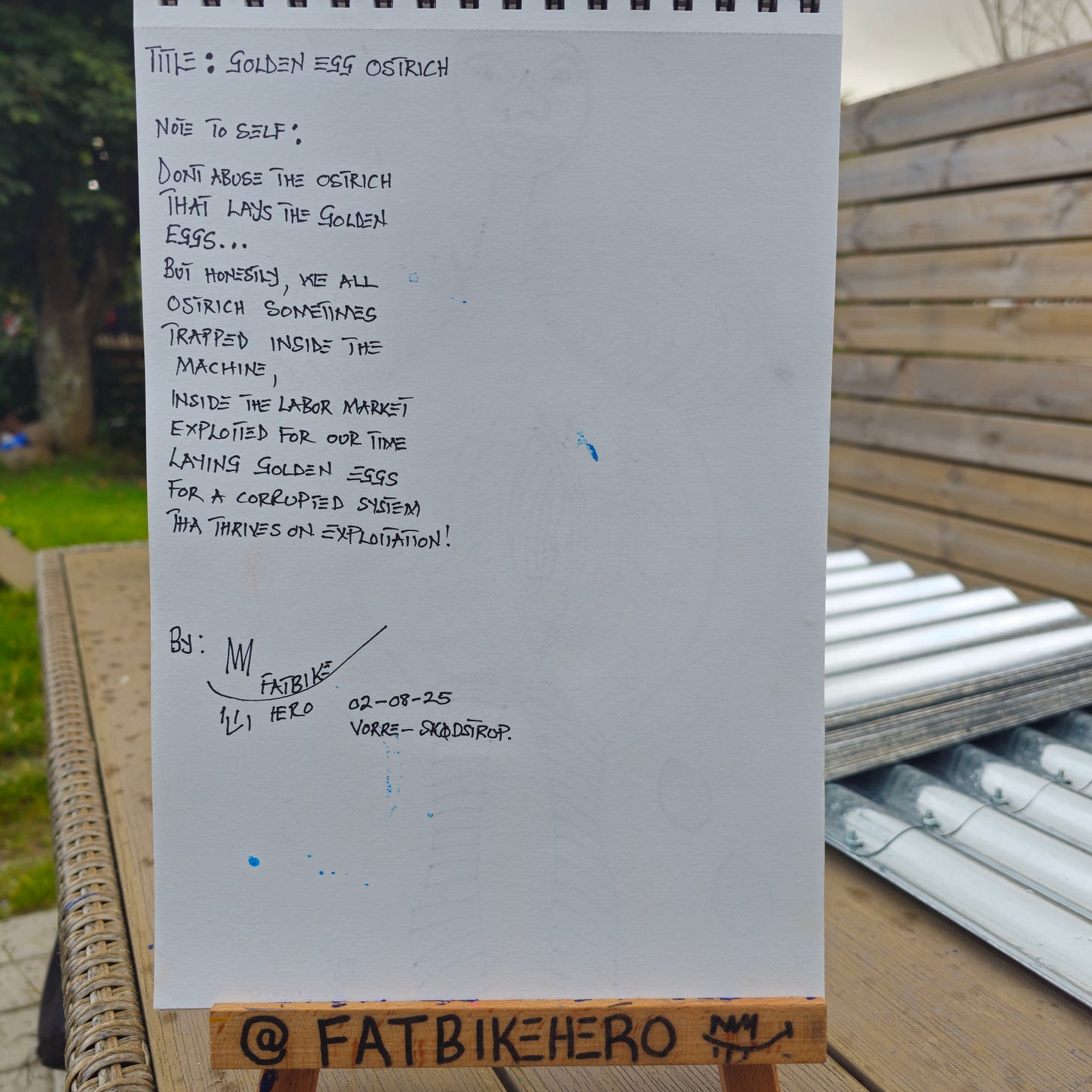 Alt Text: Handwritten artist notes in black ink on a sketchbook page by FatbikeHero. The text reads 'Title: Golden Egg Ostrich' and includes a poem about the labor market, abuse, and the 'corrupted system' of exploitation. It is signed and dated 02-08-25, Vorre-Skødstrup. Alt Text: Handwritten artist notes in black ink on a sketchbook page by FatbikeHero. The text reads 'Title: Golden Egg Ostrich' and includes a poem about the labor market, abuse, and the 'corrupted system' of exploitation. It is signed and dated 02-08-25, Vorre-Skødstrup.