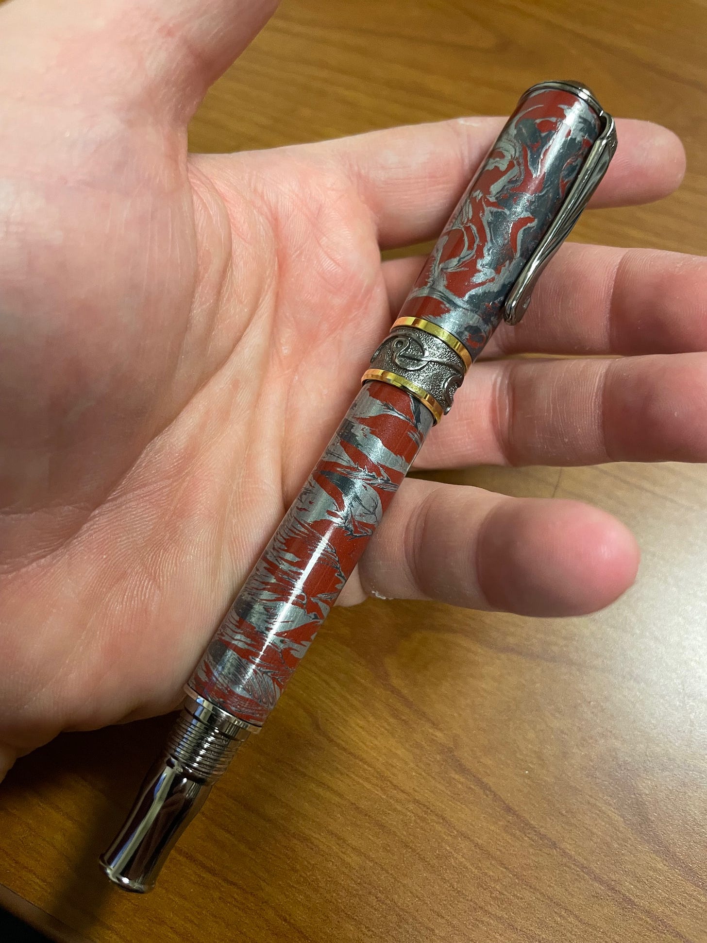 A pen with a red, blue, and silver barrel, resting in a hand.
