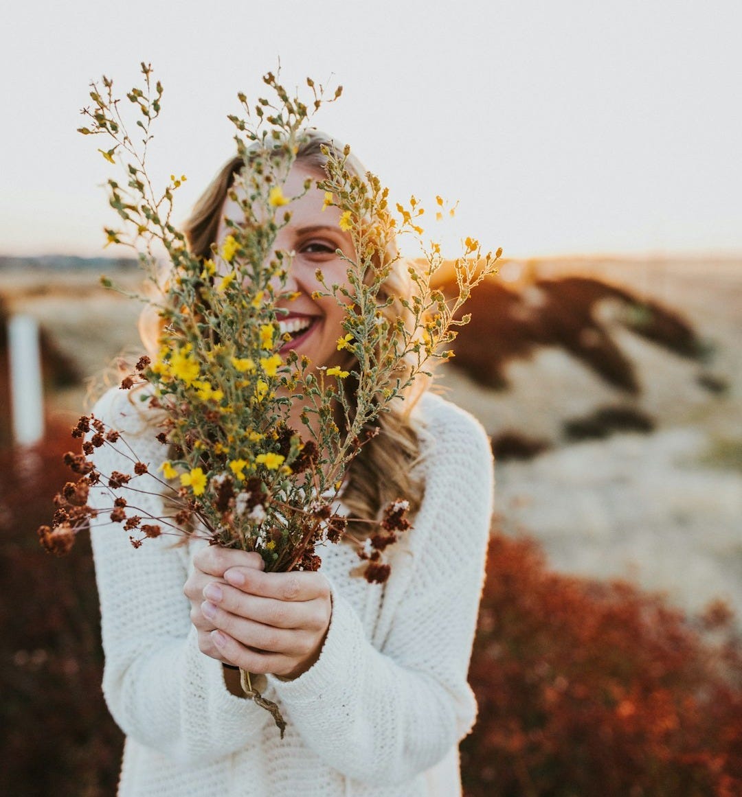 woman in white sweater holding yellow flowers