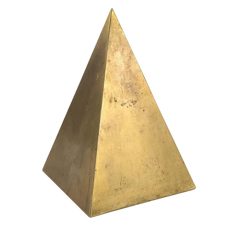 May include: A solid gold pyramid shaped object with a smooth surface.