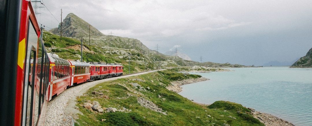 red train on rail near body of water during daytime red train on rail near body of water during daytime