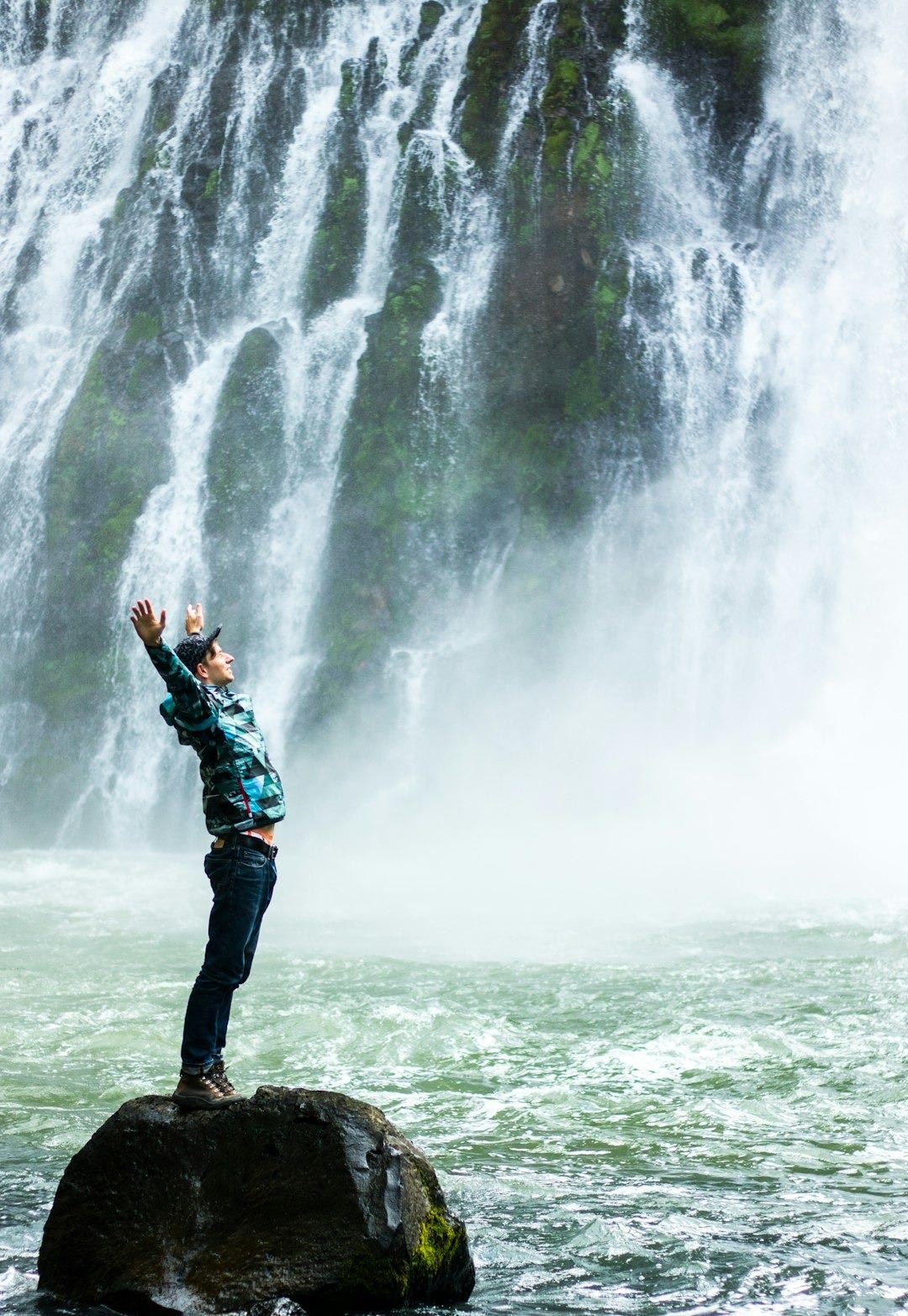 man standing on black rock surrounded body of water