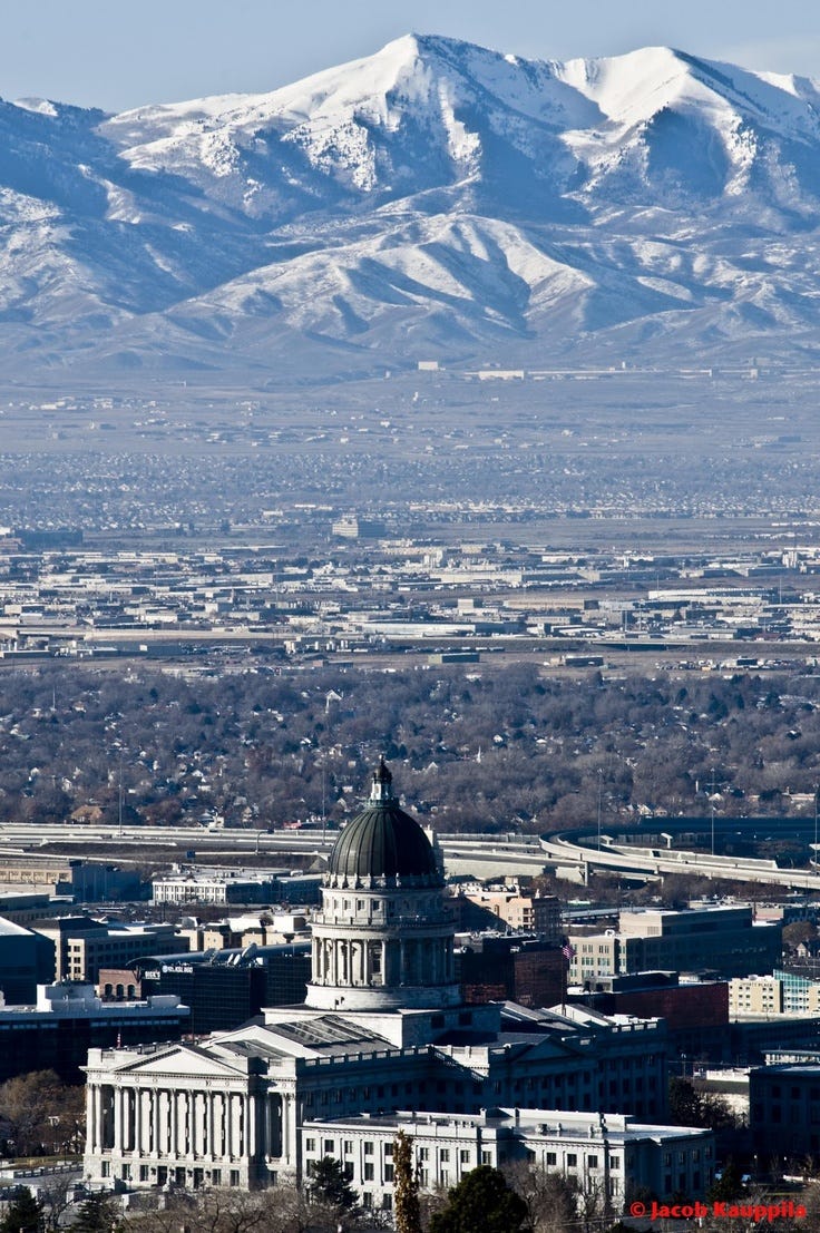 This may contain: the city is surrounded by mountains and snow capped hills in the distance, with a clock tower on top