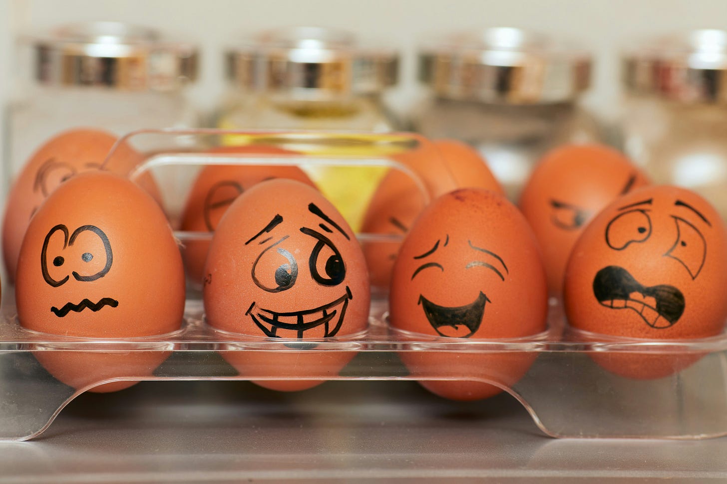 A transparent egg box shows six brown eggs on which cartoon faces have been drawn with a black marker pen, giving them diverse expressions of emotion including joy, confusion, fear. A transparent egg box shows six brown eggs on which cartoon faces have been drawn with a black marker pen, giving them diverse expressions of emotion including joy, confusion, fear.