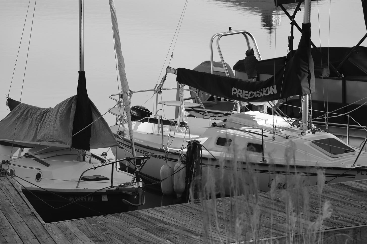 Two tiny sailboats docked on a calm lake, in black and white.
