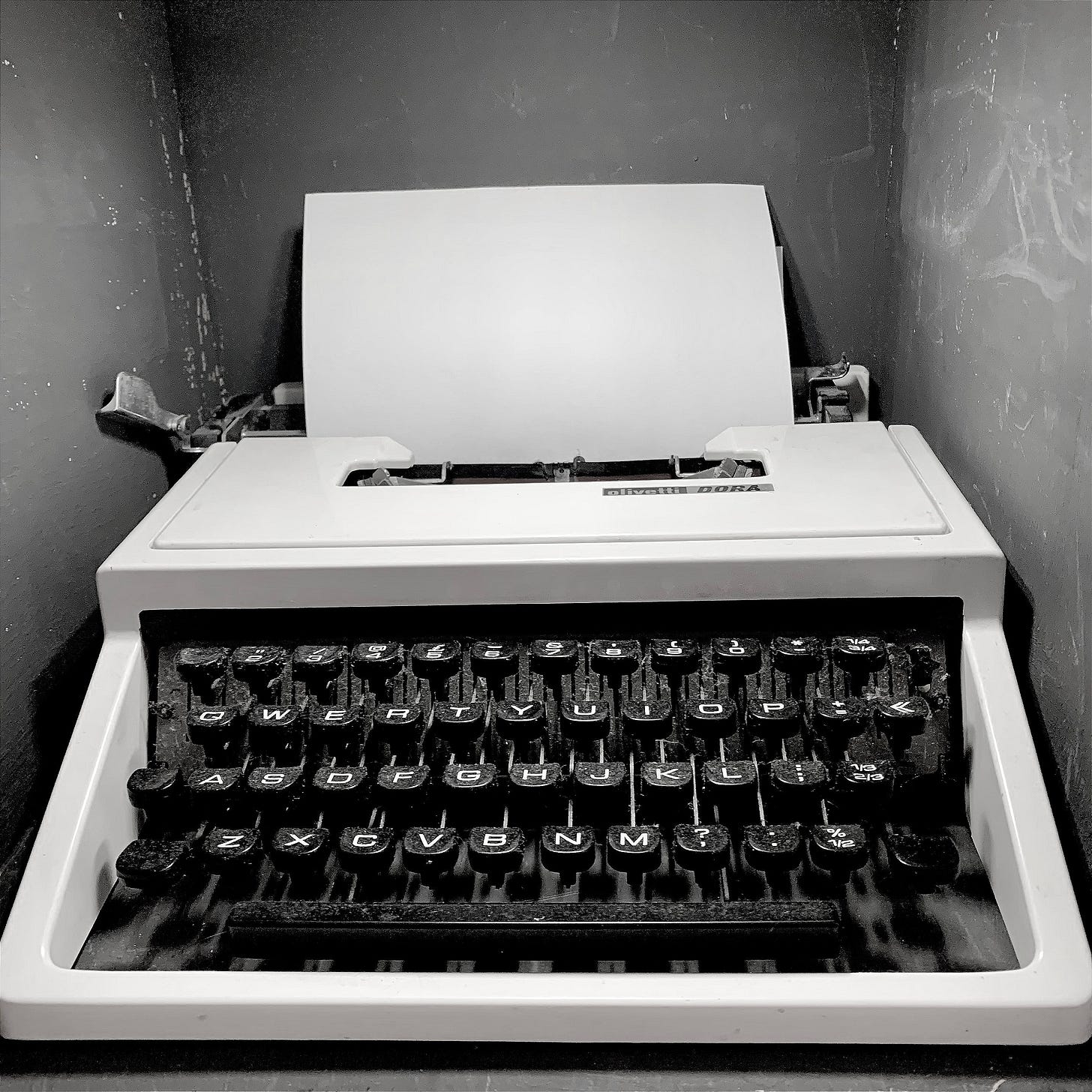 A black and white photo of a vintage Olivetti Dora typewriter, with a blank sheet of paper inserted.