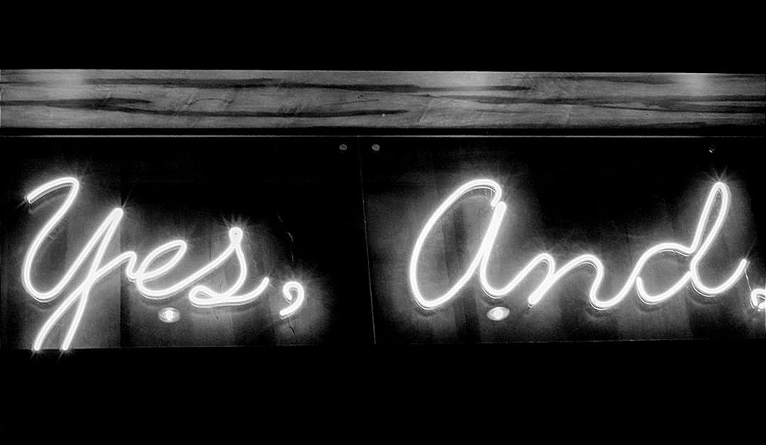 Yellow neon sign reads "yes, and." Yellow neon sign reads "yes, and."
