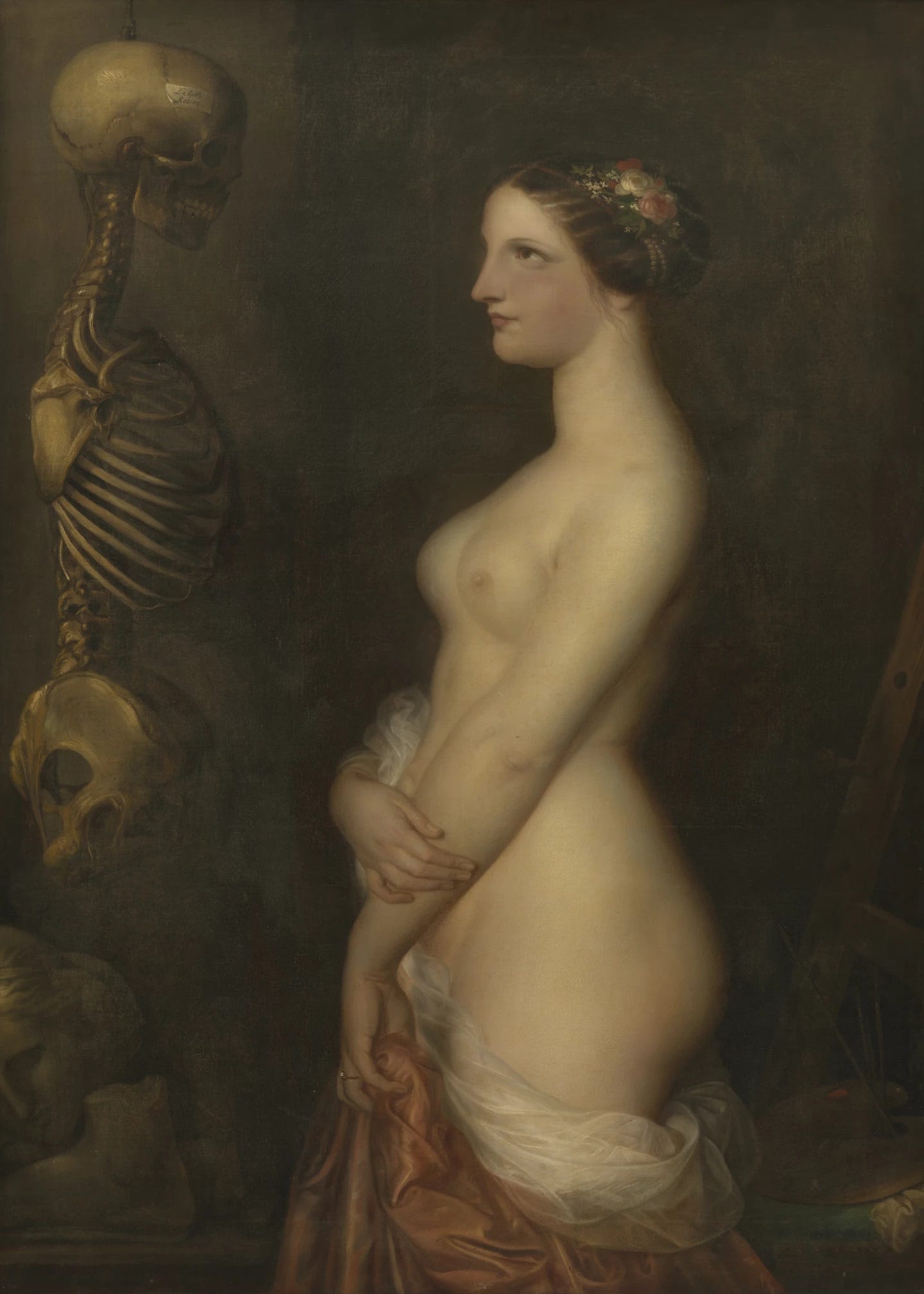 A young nude woman with roses in her hair stands in profile, holding a drape at her hip, and stares at a skeleton hanging from a hook, with a small paper label on the skull and an easel and a palette in the shadows behind her. A young nude woman with roses in her hair stands in profile, holding a drape at her hip, and stares at a skeleton hanging from a hook, with a small paper label on the skull and an easel and a palette in the shadows behind her.