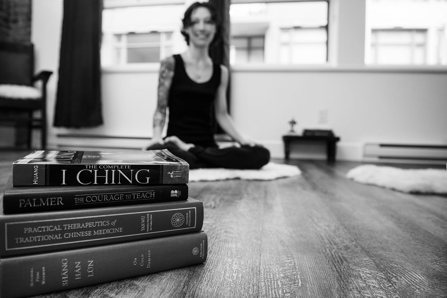 Author seated in lotus posture, smiling, with longer hair; a stack of Chinese Medicine textbooks in the foreground.